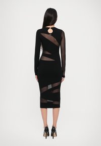 Abito nero a maniche lunghe con inserti trasparenti, silhouette aderente e dettaglio a occhiello sulla schiena. Il tessuto texturizzato mette in risalto gli elementi di design.