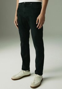 Zwarte denim jeans met een slim fit, voorzien van standaard zakken en een licht gebrusht textuur. Gecombineerd met witte lage sneakers.