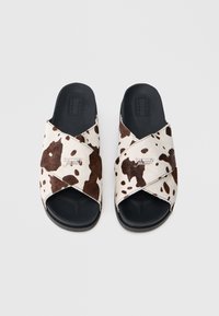 Σανδάλια τύπου slip-on με μοτίβο αγελάδας, διαθέτουν σχέδιο με σταυρωτές λωρίδες από μαλακό υλικό, μαύρες λαστιχένιες σόλες και ραμμένη λεπτομέρεια στο χείλος.