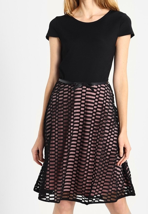 Svart tajt topp med korta ärmar, kombinerad med en utsvängd, lager-på-lager kjol med ett mönster av rosa ränder och ett svart galleröverdrag.