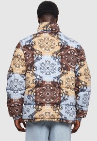 Jakna na napuhavanje s plavim, smeškim i bež patchwork uzorkom koji sadrži složene cvjetne uzorke i visoki ovratnik. Mekana, quilted tekstura.
