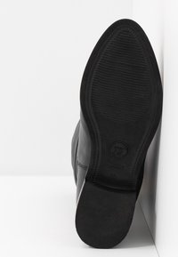 Suola di scarpa in pelle nera con grip testurizzato, logo e numero di taglia visibili, fotografata in posizione verticale su sfondo bianco.