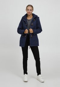 Parka bleu marine avec capuche, dotée de fermetures à bascule en bois, de poches latérales et d'une surface légèrement texturée.