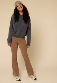 Koolgrijze sweatshirt met decoratieve studs, gecombineerd met bruin corduroy flared pants, en beige sneakers met grijze accenten.