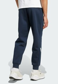 Granatowe dresy wykonane z miękkiego materiału, z elastycznymi mankietami, bocznymi kieszeniami i białym logo na dolnej części nogawki.