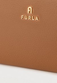 Brūna ādas rokassoma ar teksturētu virsmu un priekšpusē iegravētu zelta "FURLA" logotipu. Gludas malas un izsmalcināts dizains.