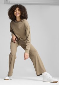 Felpa marrone a costine con cappuccio regolabile, abbinata a pantaloni a zampa coordinati. Sneakers bianche con piattaforma, suola testurizzata e dettaglio del logo.