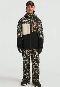 Skijack en -broek in zwart, wit en beige camouflagepatroon, met een oranje ritssluiting, geïsoleerde stof en gewatteerd ontwerp.