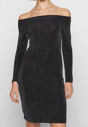 Schwarzes Schulterfreies Kleid mit langen Ärmeln und silbernen Glitzerdetails, knielang mit leichtem Seitenschlitz, getragen von einer stehenden Person.