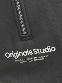 Musta huppari, jossa on vetoketjullinen etuosa, johon on painettu valkoisella "Originals Studio" ja brändin yksityiskohtia. Pehmeä kangas ja yksinkertainen muotoilu.