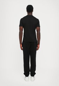 Sort bomulds t-shirt og matchende joggers set fra ryggen. T-shirten har rund hals; joggers har elastiske manchetter og sidelommer.