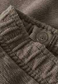 Gros plan sur un tissu tricoté brun texturé avec une ceinture élastique et un détail transparent de bouton à quatre trous.