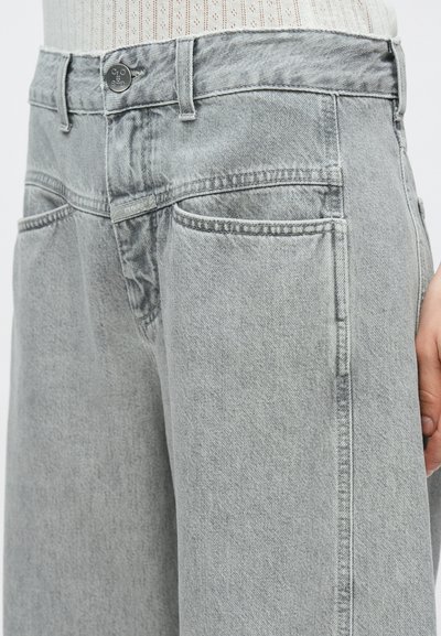 Jean en denim gris à coupe décontractée, doté d'une fermeture à boutons, de poches avant et arrière, et de détails de coutures visibles. Texture lisse.