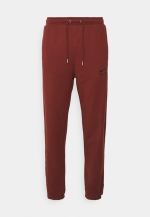 Bruine sweatpants van zacht materiaal, voorzien van een elastische tailleband met een trekkoord, omgeslagen enkels en een zwart logo-opdruk aan de zijkant.
