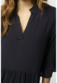 Schwarzes leichtes Kleid mit V-Ausschnitt, rüschierten Dreiviertelärmeln und gerafftem Saum. Glattes Material mit minimalen Nähten.