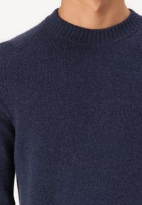 Námořnický svetr s kulatým výstřihem a žebrovaným lemem, se strukturovaným pletením, které zdůrazňuje jeho přiléhavý střih a měkkou tkaninu. Bez viditelných vzorů nebo akcentů.