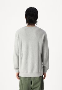 Sweater grigio a maglia con un motivo testurizzato, collo rotondo e polsini e orlo a coste, abbinato a pantaloni cargo verde oliva.