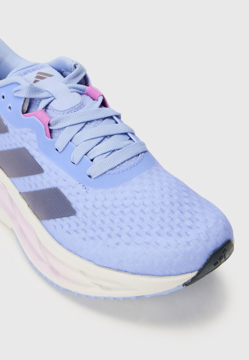 Jasnoniebieskie buty sportowe z teksturowanym wierzchem, różowymi akcentami i trzema ciemnymi paskami po bokach. Posiadają okrągłe sznurówki i wyściełaną podeszwę.