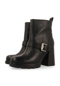 Botas de tobillo de cuero negro con tacón grueso. Cuenta con una correa con hebilla plateada y un acabado texturizado. Parte superior lisa y suela de goma duradera.