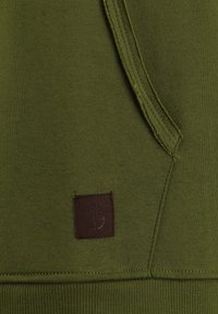 Felpa verde oliva con tessuto testurizzato, tasca laterale e una patch in pelle marrone con lettering in rilievo.