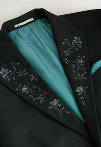 Schwarze Blazer mit floralem Stickerei am Kragen, ausgestattet mit einem tealfarbenen Satin-Futter. Das Material wirkt strukturiert mit einer glatten Textur.