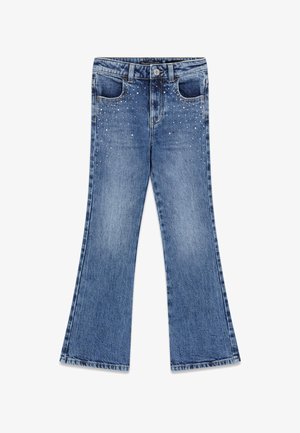 Jeans en denim bleu avec jambes évasées et petits clous argentés près des poches avant et de la ceinture.