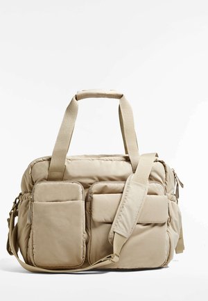 Beige padded bag with dual handles, removable shoulder strap, and multiple front pockets. Smooth texture with stitched detailing.