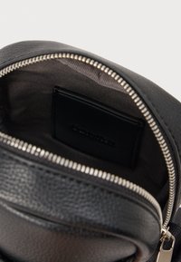 Interno di una borsa in pelle nera con una fodera a contrasto, chiusura a zip e un'etichetta. Presenta una texture liscia e un dettaglio della cerniera metallica.