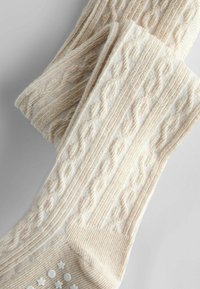 Adīti krēmkrāsas zeķes ar teksturētu kabeli un ribinātu augšu. Pamatne ir dekorēta ar mazām punktveida zvaigznēm, piešķirot saķeri un detalizētību.