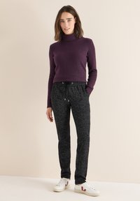 Coltrui in donkerpaars geribbeld breiwerk, gecombineerd met zwarte, gestructureerde joggingbroek met een elastische tailleband en trekkoord. Witte sneakers.