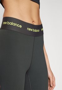 Juodos sportinės tamprės, turinčios liesą siluetą, su plačiu juosmeniu, pažymėtu "new balance" ryškiai geltonos spalvos. Sklandus, tamprus audinys su subtiliais siūlais.