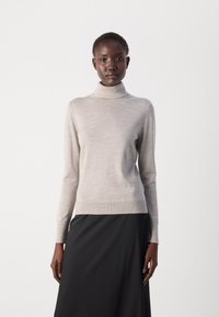 Beige sweater med høj hals lavet af fint strikket stof, lange ærmer, tætsiddende design, glat tekstur, båret sammen med en sort nederdel.