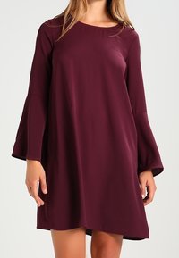 Burgundy skiftklänning med klockärmar, rundad halsringning och slät textur, med en lätt asymmetrisk fåll.