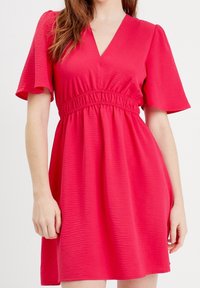 Robe courte rose avec manches courtes évasées, encolure en V et taille élastiquée. Tissu texturé avec une coupe décontractée, se terminant au-dessus du genou.