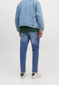 Vaaleansininen farkkutakki vihreän paidan päällä, yhdistetty vaaleansinisiin farkkuihin ja valkoisiin tennareihin. Farkkumateriaali on klassisen mallinen, jossa on ompelut.