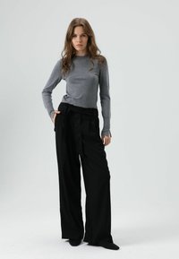 Grijze nauwsluitende top met lange mouwen en hooggetailleerde zwarte wijde broek met strikceintuur. Soepele textuur, minimalistisch ontwerp.