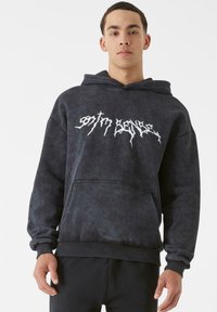 Tamsiai pilka kapucha iš minkštos medžiagos, su dideliu baltu grafiniu spaudiniu. Su priekinėmis kišenėmis ir įgleivintomis rankogaliais bei apačia.