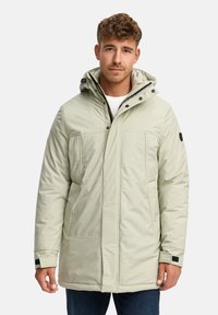 Lys grønn polstret parkas med hette, som har trykknapper, to frontlommer og elastiske mansjetter. Materialet ser glatt og vanntett ut.