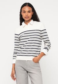 Stripet skjorte med lange ermer i krem og marineblå, med krage og oppbrettede mansjetter. Stoffet ser mykt ut; liten logo på brystet.