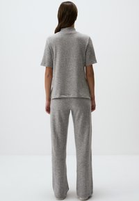 Grijze gebreide loungwear-set met een T-shirt met korte mouwen en wijde broekspijpen. De stof heeft een zachte textuur met een subtiel gemêleerd patroon.