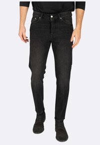 Jeans in denim nero con vestibilità slim, dotati di cinque tasche, cuciture a contrasto e dettagli in metallo. Tessuto testurizzato con leggero elastico.