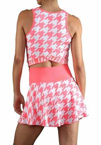 Una mujer lleva una blusa de crop top en patrón de espiga en rosa y blanco y una falda a juego con el texto "ENDLESS" en la cintura, vista desde atrás.