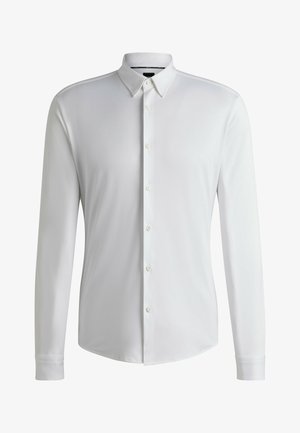 Camisa blanca de manga larga fabricada en tejido suave, con cuello puntiagudo, cierre de botones completo y dobladillo redondeado con puños abotonados.