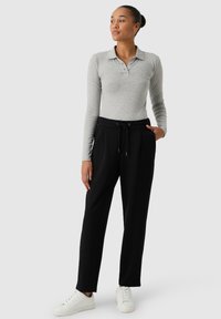 Szara koszulka polo z długim rękawem, z kołnierzykiem i trzema guzikami, w połączeniu z czarnymi spodniami dresowymi ze sznurkiem. Model nosi białe sneakersy.