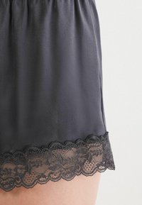 Zwarte satijnen shorts met een gathered elastische tailleband, voorzien van een decoratieve kantafwerking aan de zoom. Zachte textuur en een gladde afwerking.