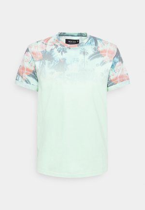 T-shirt vert clair à manches courtes avec imprimé estompé de palmiers tropicaux et de fleurs sur la poitrine supérieure et les manches.