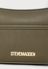 Zielona torebka z teksturowanej ekoskóry z złotym logo "STEVE MADDEN". Posiada gładki, zaokrąglony kształt z widocznymi detalami szycia.