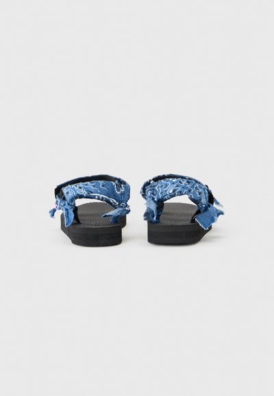 Ζευγάρι μαύρων σαγιονάρων με παχιές σόλες και μπλε υφασμάτινα λουριά με λευκά σχέδια παϊσλεϊ, απεικονιζόμενα από πίσω σε απλό φόντο.