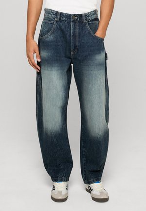 Farmernadrág laza szabással és színátmenetes kifakulással. Sötétkék a tetején, világosabb kék felé átmenettel. Első zsebekkel és cipzárral ellátva.