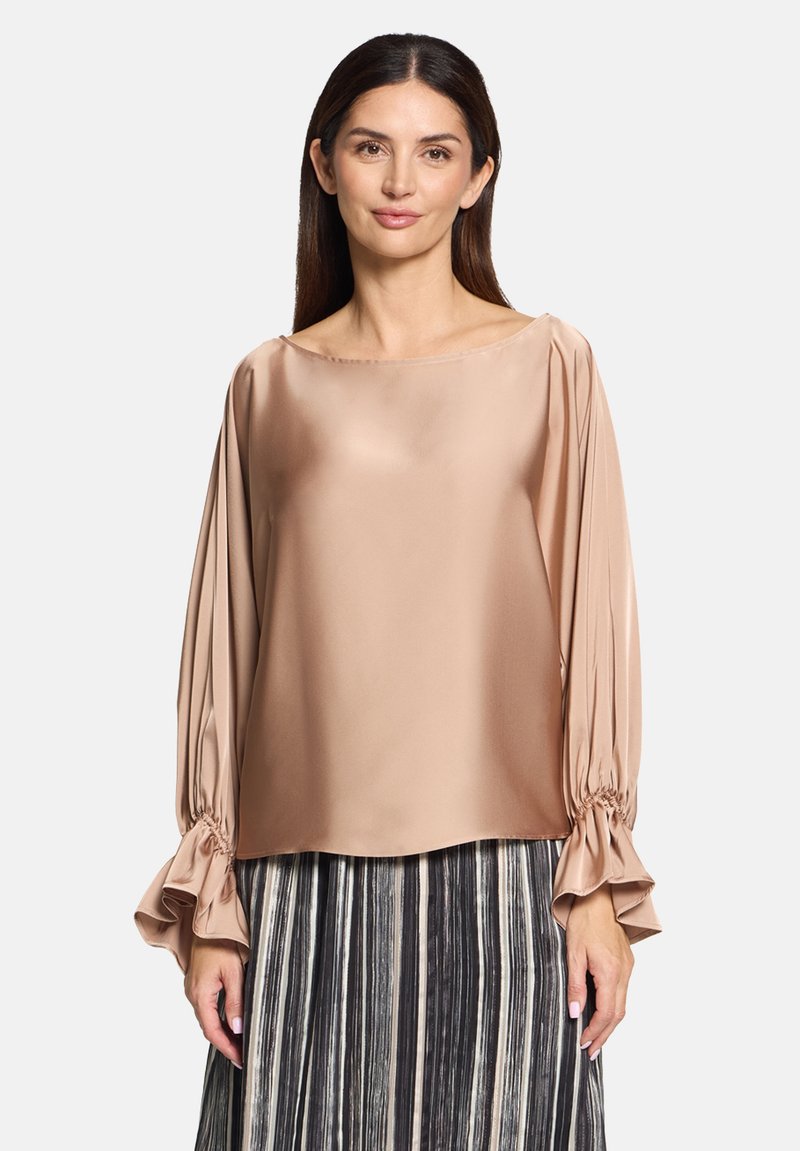 Beige satinbluse med en bred halsudskæring og gathered, udvidede lange ærmer. Stoffet har en glat tekstur med en let glans.
